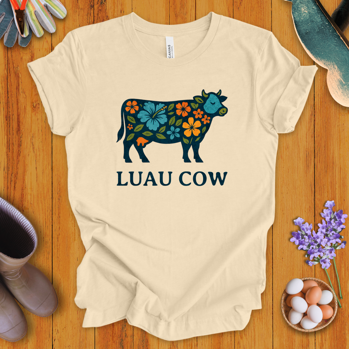 Floral luau cow graphic on soft cream t-shirt with bold text “LUAU COW”